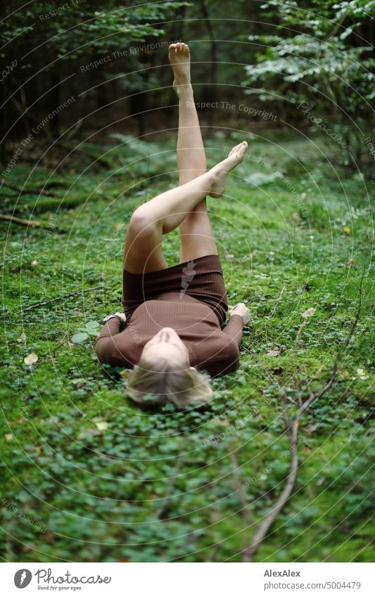 Young blonde woman lying barefoot in moss in on forest floor holding legs in air Young woman Woman Blonde Feminine pretty fortunate Youth (Young adults)