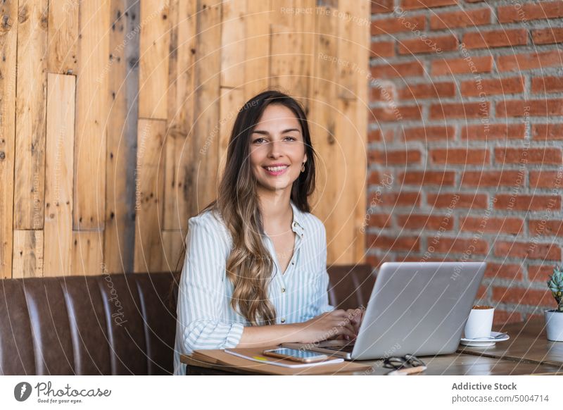 Smiling female freelancer using laptop in cafe woman smile project happy data delight remote telework table glad young smart casual workplace busy cafeteria