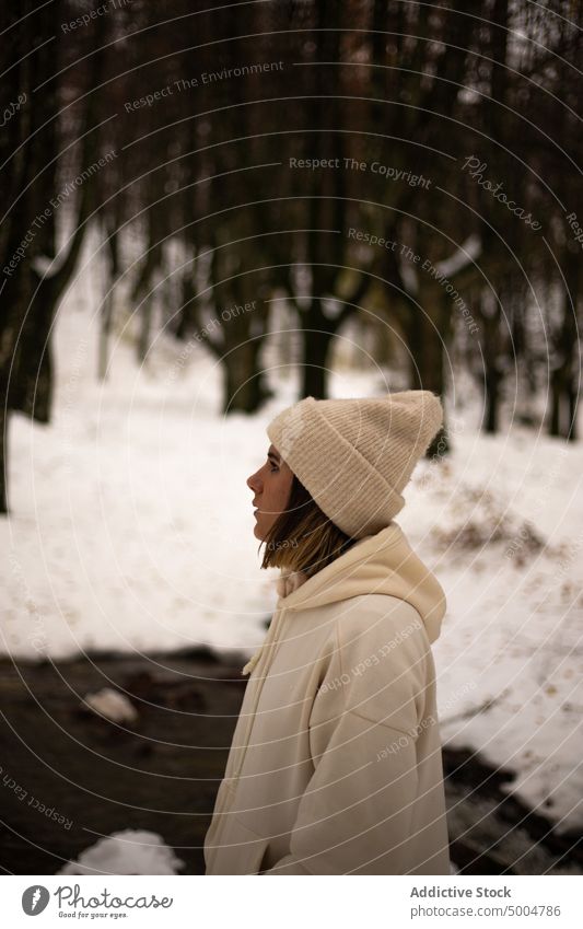 Young woman in warm clothes standing in winter woods snow cold dreamy river forest wintertime nature hat melancholy hand in pocket pensive calm woodland hoodie