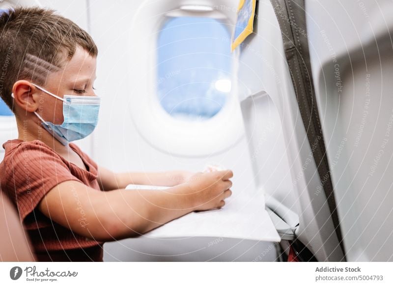 Boy using smartphone in plane boy play videogame pandemic passenger online travel covid 19 coronavirus kid transport childhood cellphone airplane trip epidemic