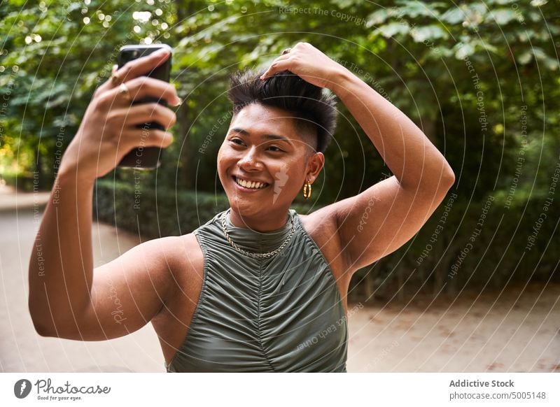 Cheerful Asian non binary person taking selfie woman transgender smile park smartphone touch hair admire reflection happy asian filipino ethnic summer weekend