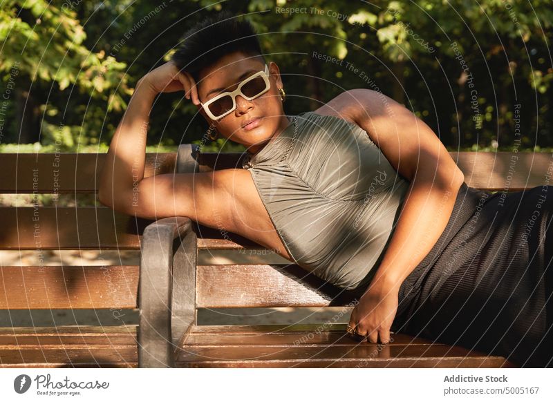 Asian non binary person lying on bench woman transgender park lgbt summer appearance lean on hand queer asian filipino ethnic weekend daytime individuality