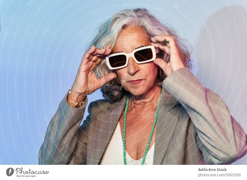 Stylish senior businesswoman under neon light confident style illuminate serious touch sunglasses appearance portrait smart casual female elderly aged gray hair
