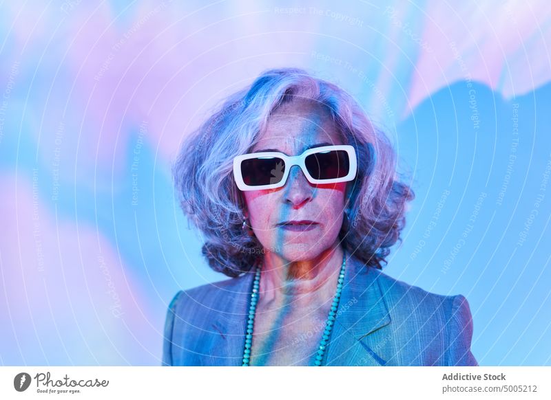 Senior woman under colorful neon light pensioner illuminate individuality portrait gray hair female elderly senior aged necklace jacket businesswoman human face