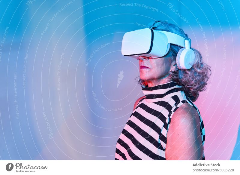 Stylish aged female in VR headset woman explore virtual reality neon colorful illuminate gamer experience cyberspace elderly senior vr pensioner retire modern