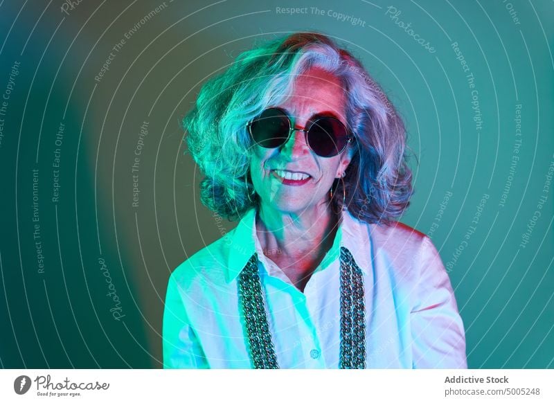 Stylish elderly woman in round sunglasses smile style appearance illuminate neon colorful portrait bright modern female gray hair senior aged pensioner retire