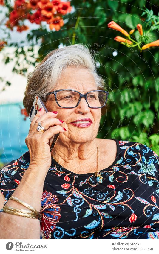 Elderly woman talking on smartphone in garden conversation smile yard flower phone call female elderly senior aged speak bush gadget green summer casual happy