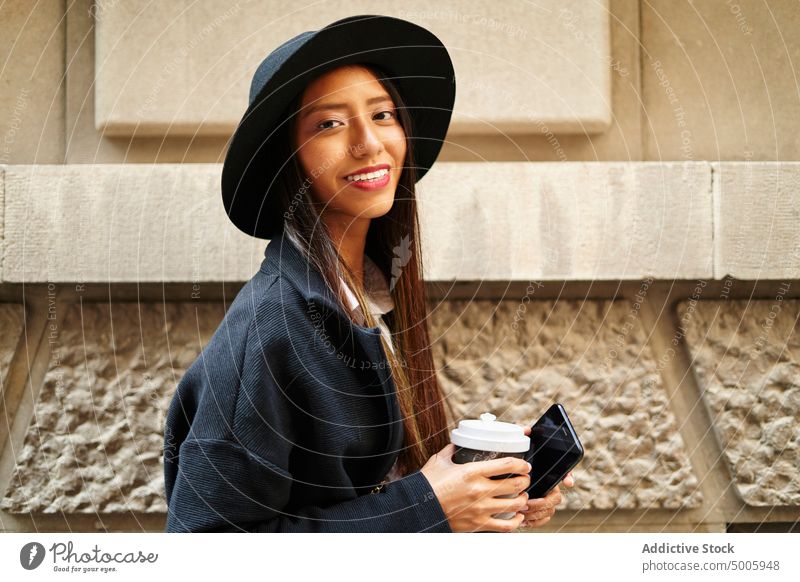 Cheerful Hispanic woman with takeaway coffee and smartphone style trendy fashion building street city cellphone smile outfit garment attire apparel charm