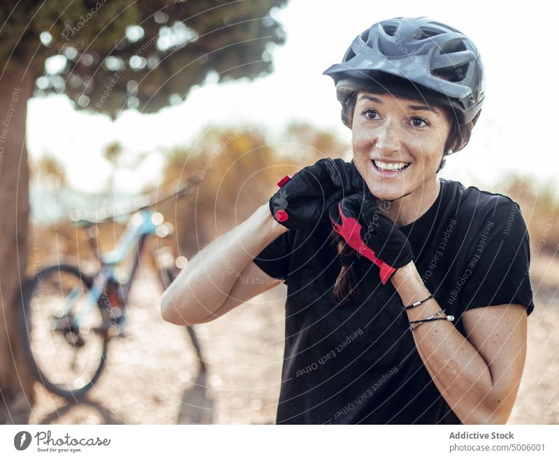 Smiling woman buttoning helmet and bike near tree sport extreme smiling bicycle activity gloves safety forest cheerful young lady attractive riding biker mtb