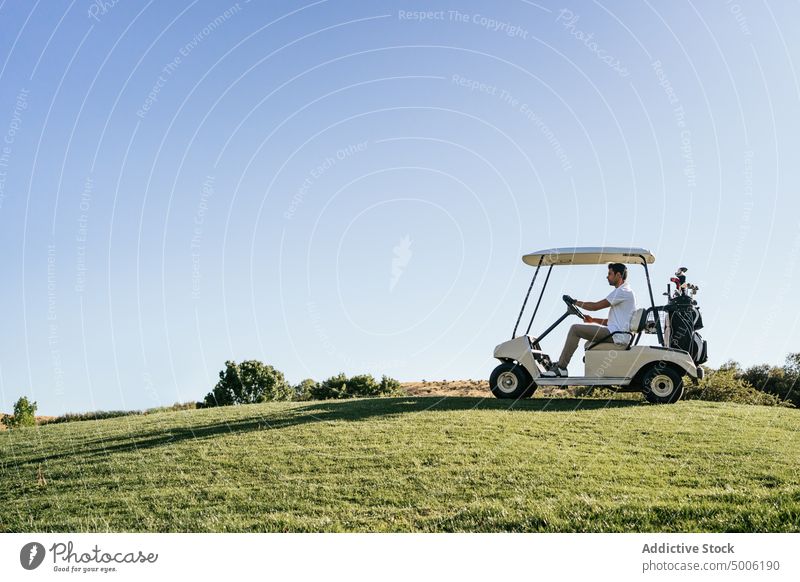 Athlete driving golf cart in green field golfer drive sport club masculine nature course man countryside vehicle transport luxury aristocratic macho small tree