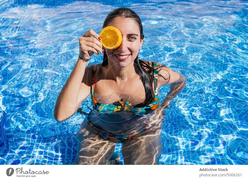 Happy woman with orange slice enjoying summertime in pool fresh tropical poolside happy fruit sunlight resort sunny water vacation female cheerful cover eyes