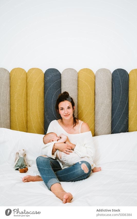 Happy mother feeding tranquil baby while relaxing on bed together at home infant kid parent eat mom harmony child comfort care newborn bedroom love milk