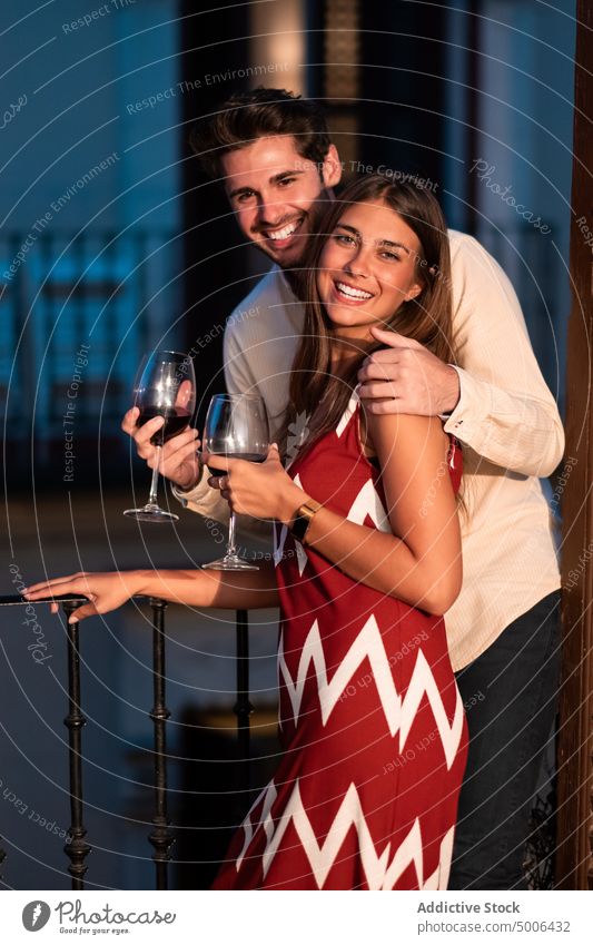 Happy couple of lovers drinking wine on balcony lean on girlfriend boyfriend together twilight enjoy romantic celebrate affection event embrace relationship