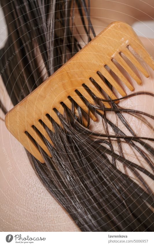Closeup of female back with wet hair strands covered with conditioner and wooden comb, bathroom beauty body care clean cleanse closeup concept faceless girl