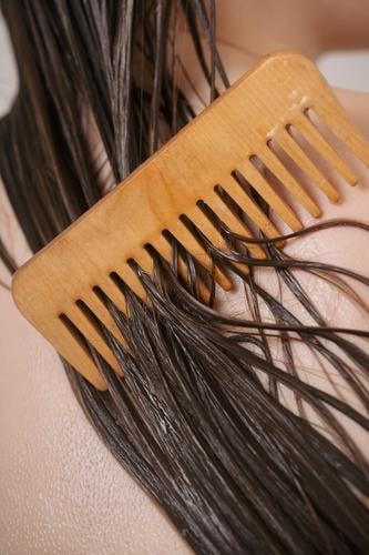Closeup of female back with wet hair strands covered with conditioner and wooden comb, bathroom beauty body care clean cleanse closeup concept faceless girl