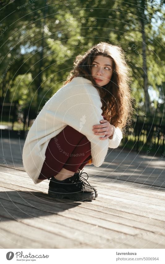 Brunette woman in a white sweater sitting in the park, selective focus adult alone attractive autumn brunette casual caucasian cheerful curly hair cute fall