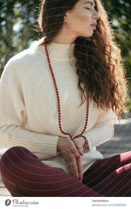 Brunette woman in a white sweater meditating in a park, selective focus Mala beads adult alone attractive autumn brunette casual caucasian curly hair cute fall