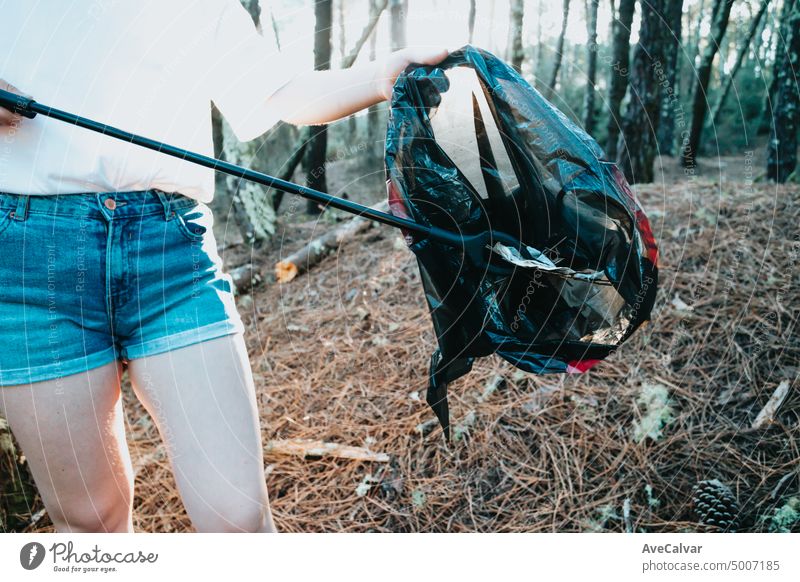 Photo of side of girl picking up garbage in bag on the forest during a sunset.Environmental garbage pollution.Nature cleaning, volunteer ecology green concept.