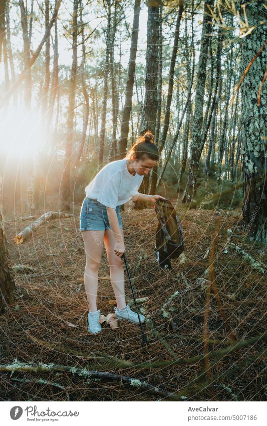 Photo of side of girl picking up garbage in bag on the forest during a sunset.Environmental garbage pollution.Nature cleaning, volunteer ecology green concept.