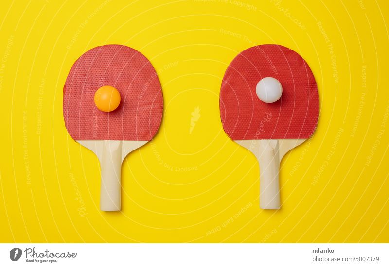 Pair of wooden tennis rackets for ping pong on a yellow background ball sport game equipment leisure competitive paddle play recreation red challenge handle