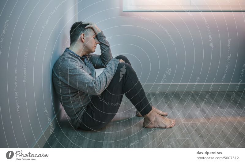Man with problems resting sitting on the floor man guy stress tired desperate head arms copy space closed eyes anxiety sad lonely depression crisis recession