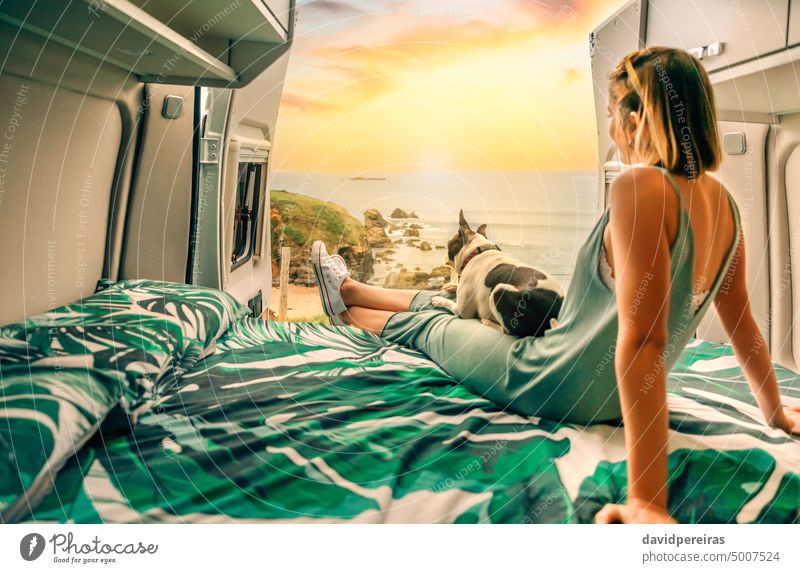 Woman with her dog watching the sunset sitting on the bed of her camper van young woman unrecognizable faceless anonymous boston terrier back trip pet vacation