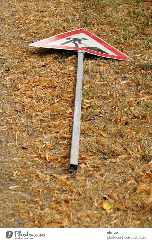 road sign lying on the dried up lawn - caution construction site - / construction site sign Road sign Caution construction site VZ 123 Vandalism Termination