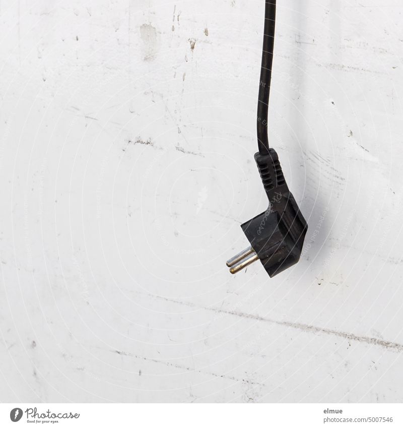 a pulled black plug hangs down on an electrical device / save power Connector pulled plug save electricity electricity price switched off