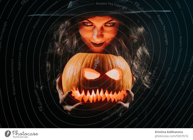 Mysterious black witch with pumpkin as head of jack-o-lantern on dark backdrop. Scary symbol of Halloween, masquerade costume, party decoration. Magic, classic hag