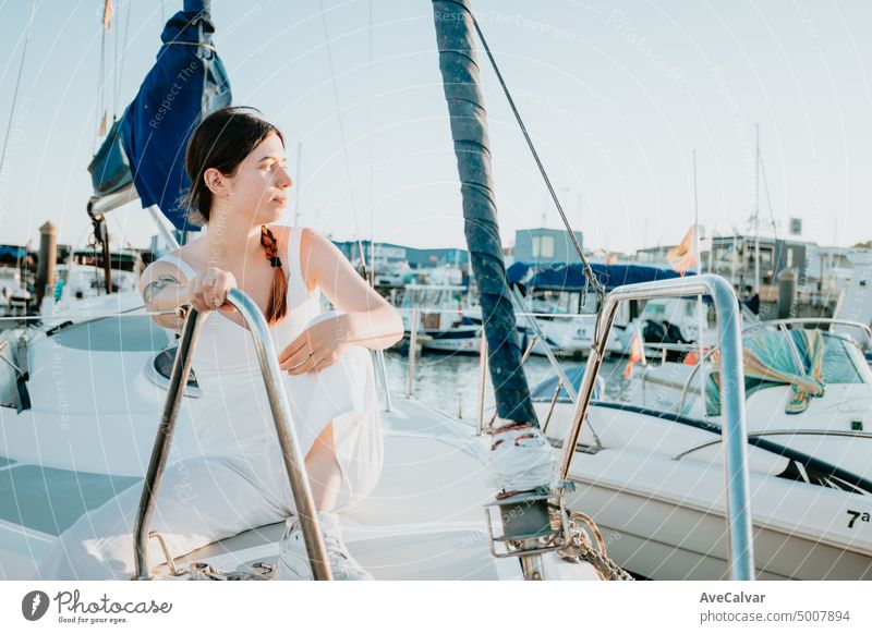 Young happy woman having fun on the luxury sail boat during her summer holidays. Calm young lady sitting on sailboat. Getting the boat ready to sail. Vacation, youth and fun concept