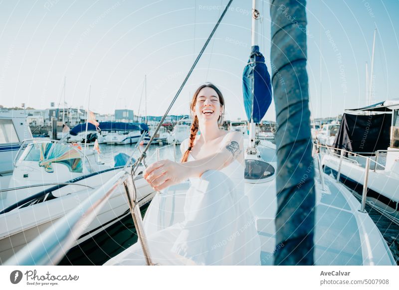Young happy woman feels fun on the luxury sail boat during her summer holidays. Calm young lady sitting on sailboat. Getting the boat ready to sail. Vacation, youth and fun concept