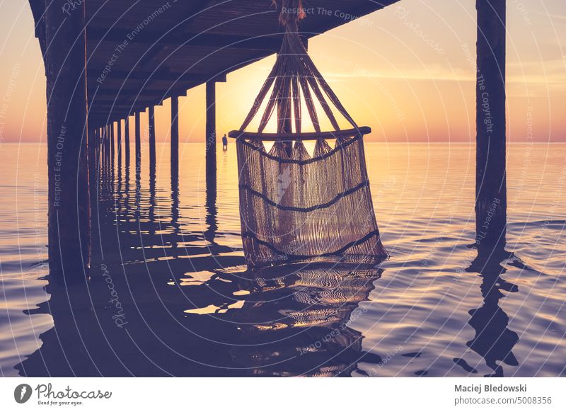 Silhouette of a hammock in water under a pier at sunrise, color toning applied. sunset silhouette sea vacation summer island beautiful nature getaway tropical
