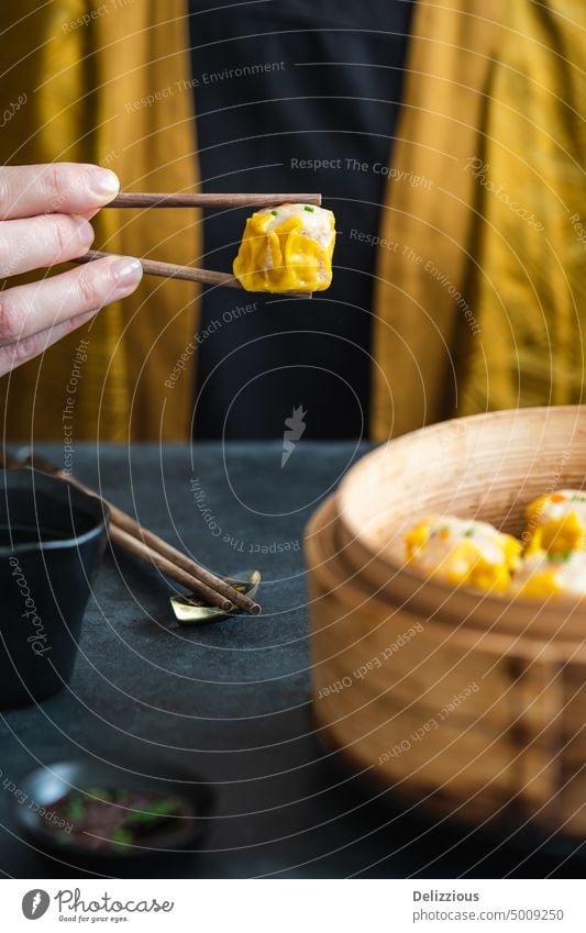 A woman in yellow kimono holding a dim sum with chopsticks asian starter food epicure appetizer one steamed basked hand person prepared many vertical one person