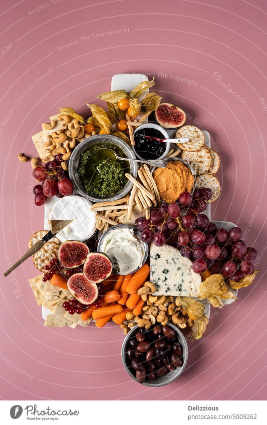 A beautiful cheese platter board with fruit, vegetables, dips and nuts on a pink background, vertical antipasto camembert carrots cheese board cheeseboard