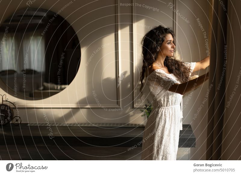 Young curly hair woman standing by the window in the room apartment beautiful beauty casual caucasian elegant enjoy face fashion female femininity fun gorgeous