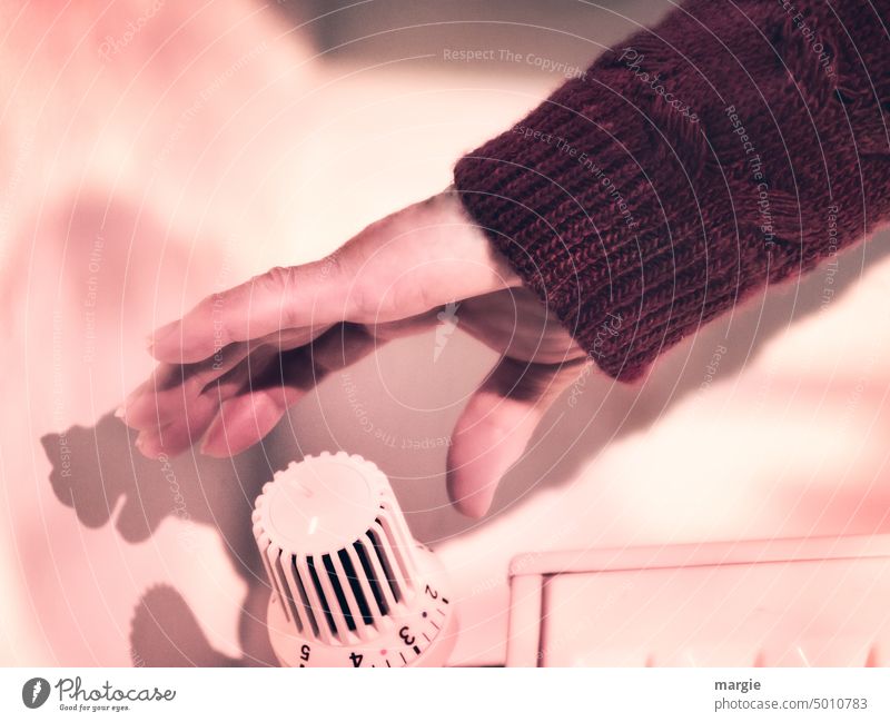 One hand reaches for the heating thermostat Hand Heater Warmth Sweater Heating Save energy heating costs Energy Temperature warm Cold Expensive Gas