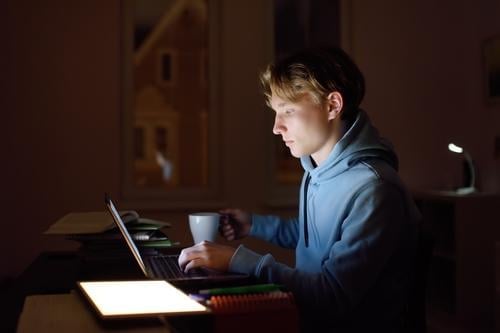 Concentrated teenager studying late night at home office with laptop and tablet. student online university internet self-employed work learn workplace