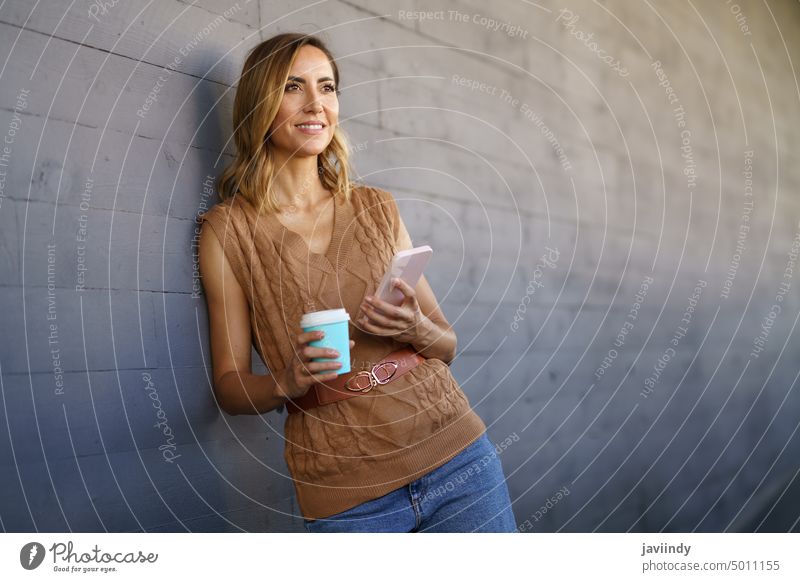 Middle-aged woman taking a coffee break. Caucasian woman using a paper cup and holding her smartphone. Woman middle age Snack bar Coffee Paper Cup Drinking