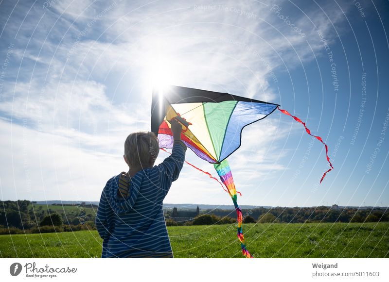 Boy from behind with striped hoodie and view over fields and meadows flying a colorful kite climb the kite Boy (child) Autumn variegated Rainbow free time