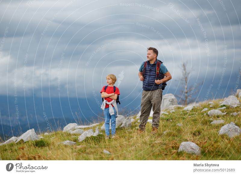 Cute schoolchild and his mature father hiking together on mountain and exploring nature. Concepts of adventure, scouting and hiking tourism for kids. hike