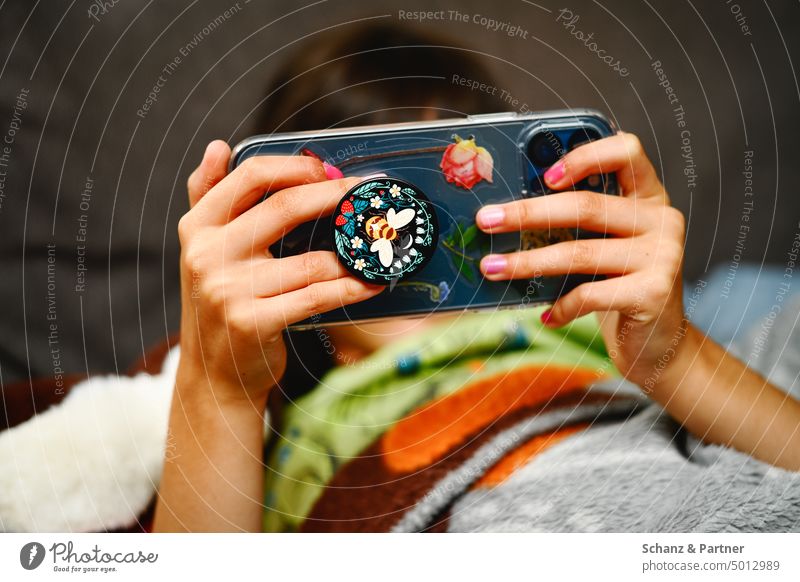 Child with painted fingernails looks at smartphone covered with stickers hands Hand To hold on Cellphone streaming Digital Internet social media Media youtube