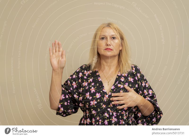 Beautiful elegant caucasian woman on a beige isolated background. Swearing with hand on chest and fingers, taking a pledge of allegiance oath. gesture justice