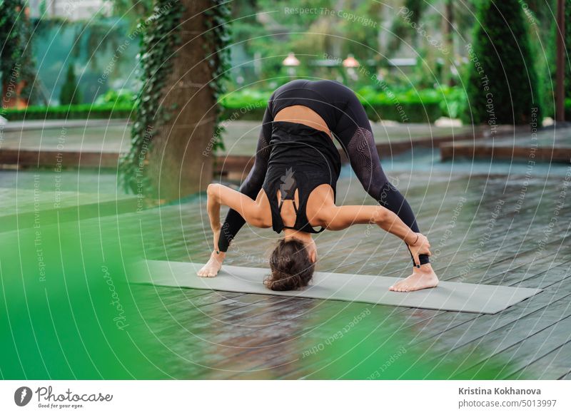Professional gymnast fitness instructor doing Uttanasana standing barefoot on yoga mat. Flexible woman stretching forward, head inclination to legs. healthy lifestyle concept