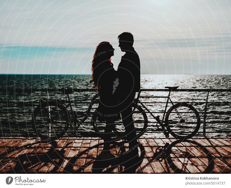Silhouettes of couple near bicycles on sea embankment. Girl and boy on date. People and healthy lifestyle concept. Romantic scene. young woman fitness together