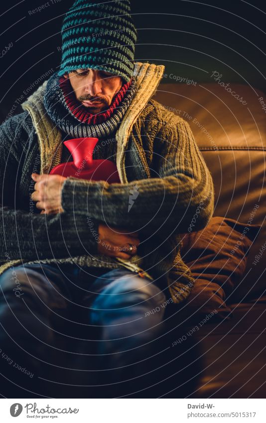 freezing man warmly dressed with hot water bottle on the sofa of his apartment Freeze Cold Man at home Flat (apartment) heating costs Save Hot water bag