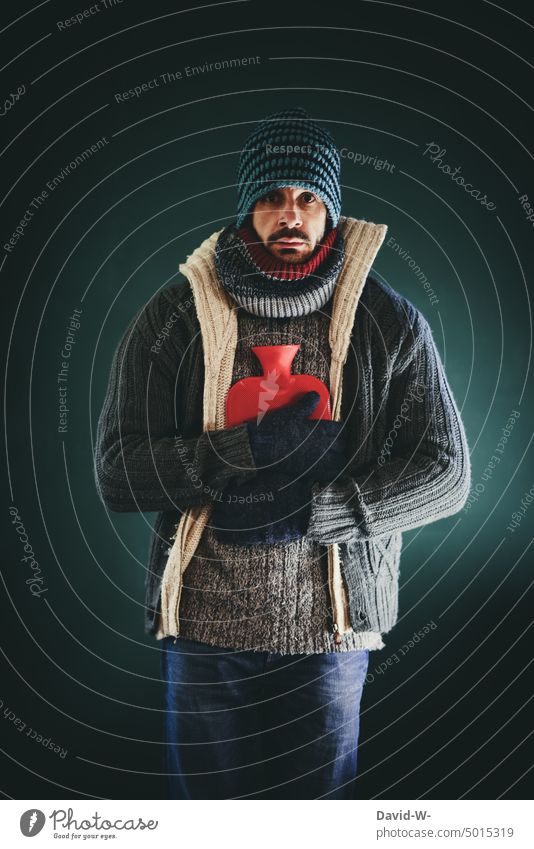 warmly dressed man with hot water bottle freezes at home Freeze Man inflation concept heating costs energy costs Save Cold Hot water bag Winter Energy crisis