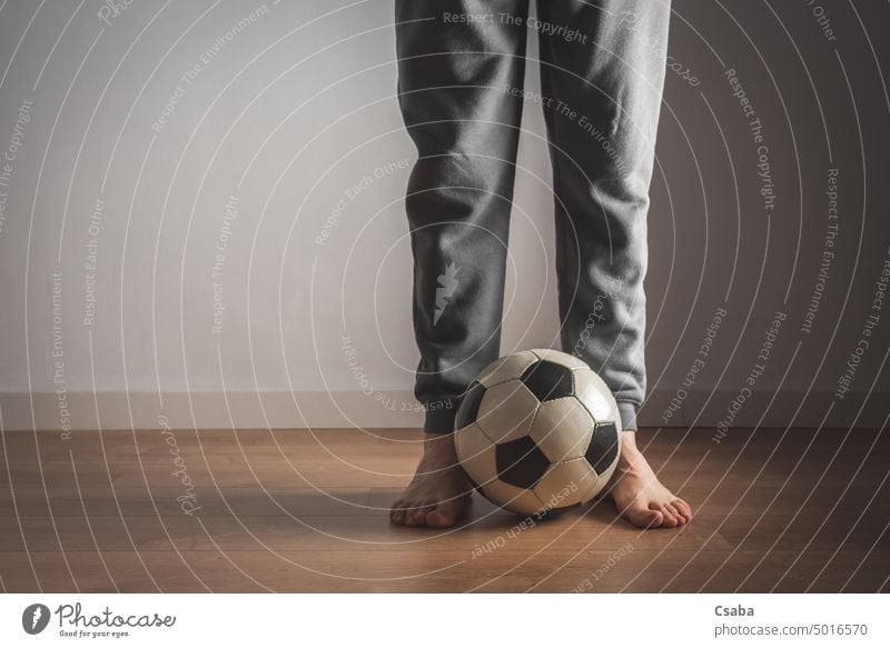 Legs of a man standing in front of a football soccer legs room indoors barefoot feet male unrecognizable adult person next to sports white wall people active