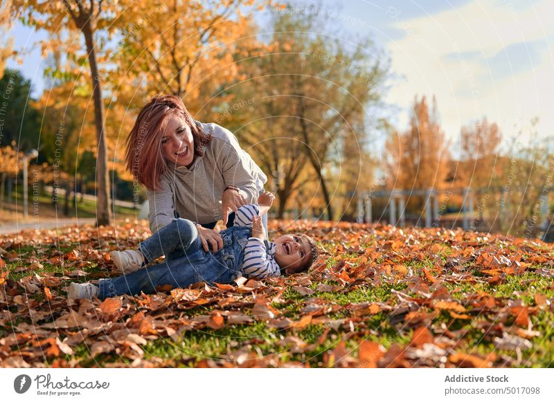 Happy mother tickling little son in park in fall tickle child having fun play playful cheerful autumn laugh spend time together kid parent motherhood childhood