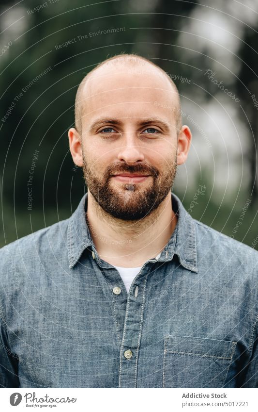Smart bearded man in denim shirt looking at camera handsome park stylish human face portrait male young relax adult calm day nature bald confident model