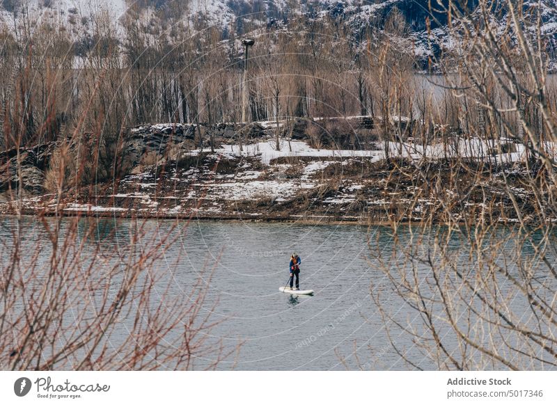 Man on paddle board between water and mountains on coast man floating tourist surface hill sup snow shore winter picturesque view stone nature travel landscape